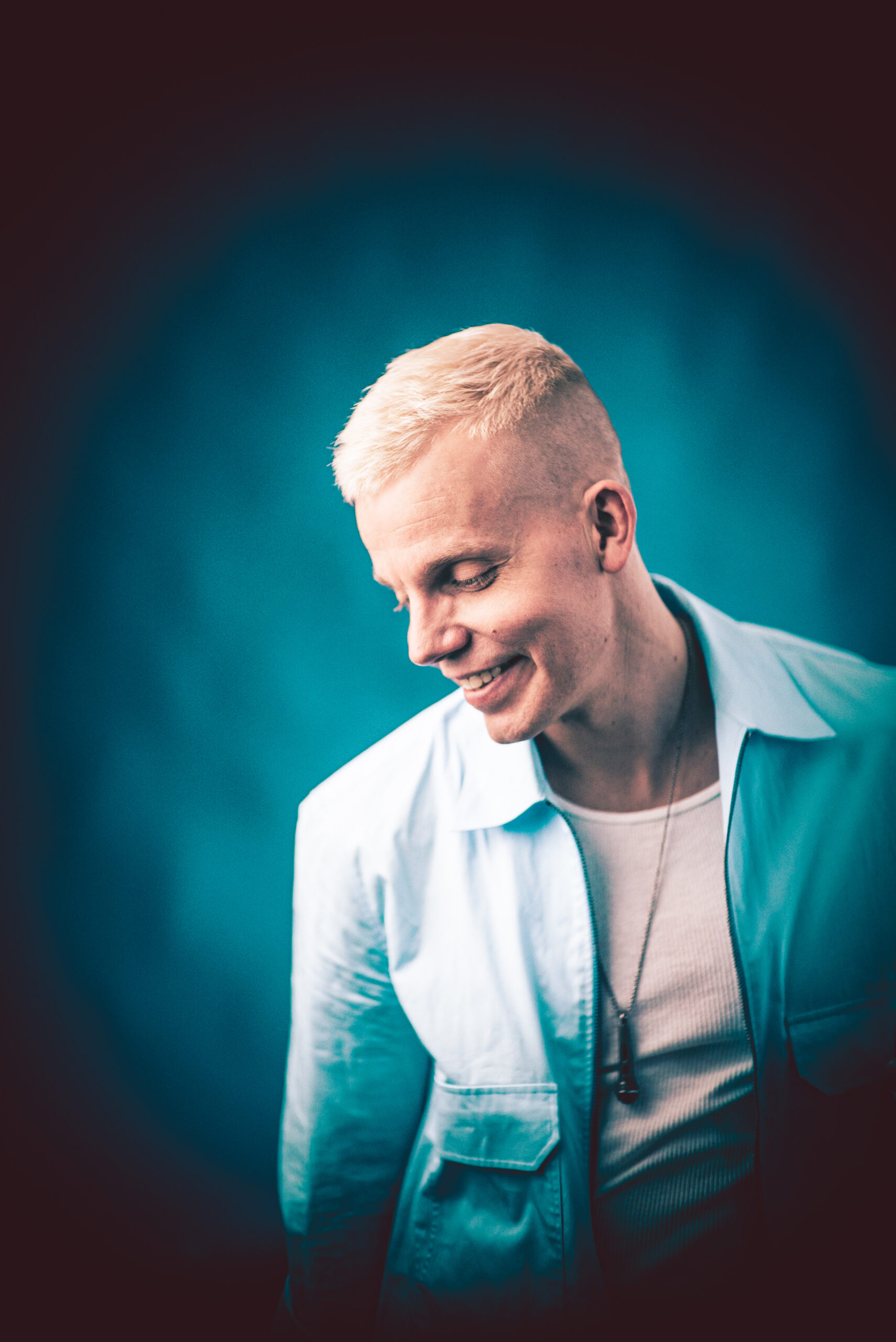 Sinisävyinen promokuva artistista Elastinen, jossa artisti hymyillen katsoo alaviistoon